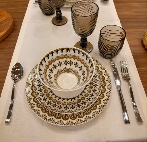 A high-angle shot of a patterned tea cup with its plates and other tableware on the table