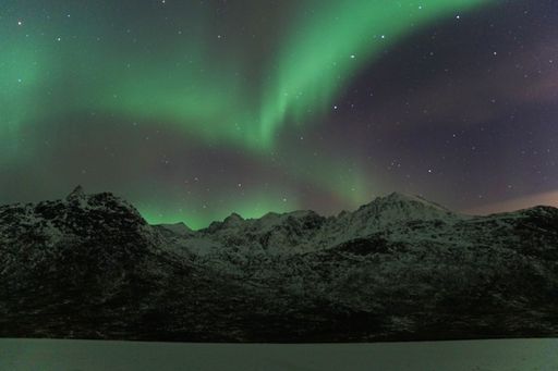The beautiful Aurora Borealis over mountain and lake water in Kvaloya, Arctic region in Norway