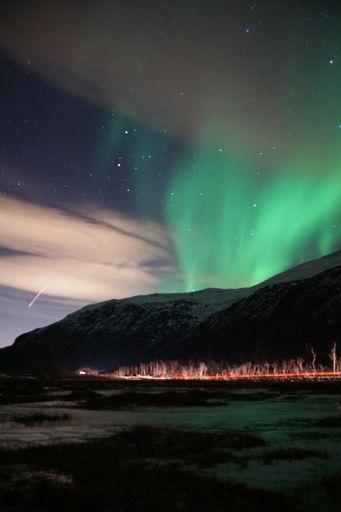 The breathtaking Aurora Borealis over mountain and lake water in Kvaloya, Arctic region in Norway