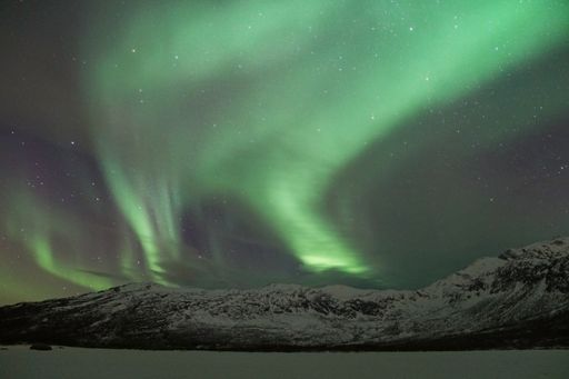 The breathtaking Aurora Borealis lights over a snowy mountain in Kvaloya, Arctic region in Norway