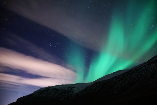 The beautiful Aurora Borealis green lights over a snowy mountain in Kvaloya, Arctic region, Norway