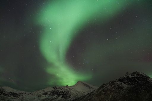 A night starry sky with Aurora Borealis lights over snowy mountain in Kvaloya, Arctic region, Norway
