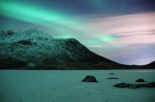 A night starry sky with Aurora Borealis lights over snowy mountain in Kvaloya, Arctic region, Norway