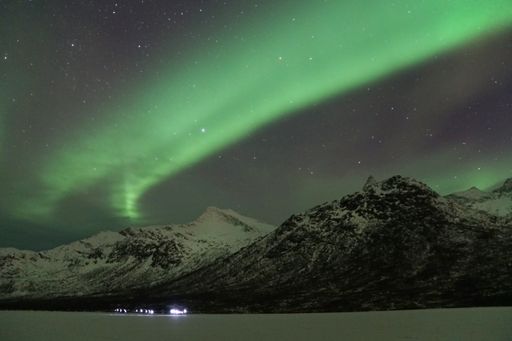The beautiful Aurora Borealis green lights over a snowy mountain in Kvaloya, Arctic region, Norway
