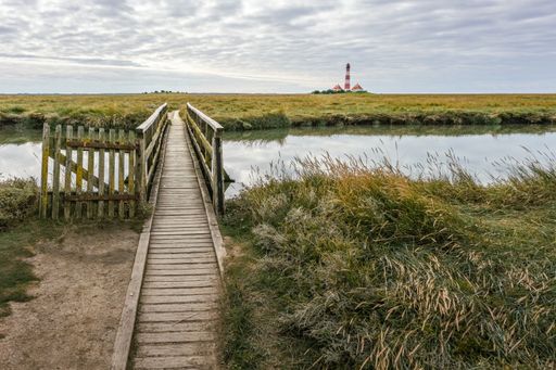 A wooden pier with Lighthouse Westerhever in west coast of northern Germany on the background