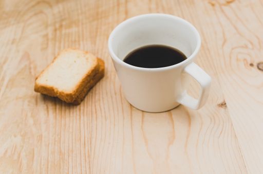 black coffee in a white mug and rusks on a rough wooden background with space for text