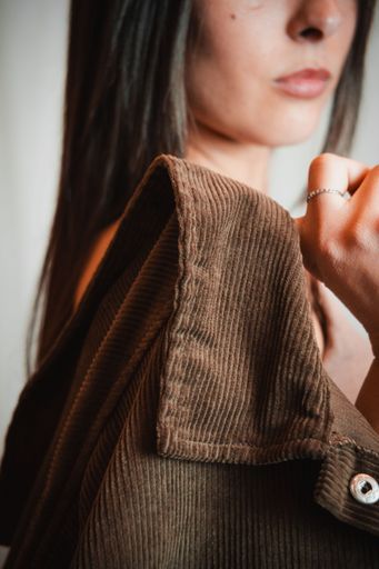 Close-up of a young woman holding a brown corduroy jacket, focusing on texture and fashion detail.