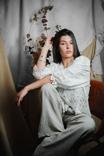 A vertical shot of a stylish young Latina woman in vintage lace and gray trousers, posed thoughtfully in a studio setting
