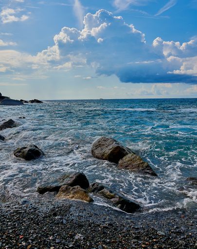 A vertical shot of a beach with rocks washed by waves under a bright cloudy sky in Italy