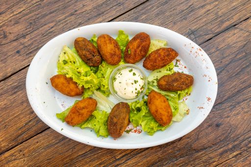 A top view of falafel with sauce and lettuce served in a white plate on a wooden table