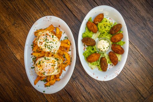 A top view of French fries with egg pashot and falafel with sauce served in a white plates on a wooden table
