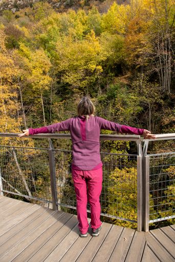 A vertical shot of the young woman standing on the viewpoint in the autumn forest. Canillo, Andorra.