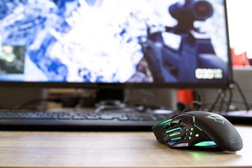 A gaming Trust Gaming mouse in front of a keyboard and a PC screen
