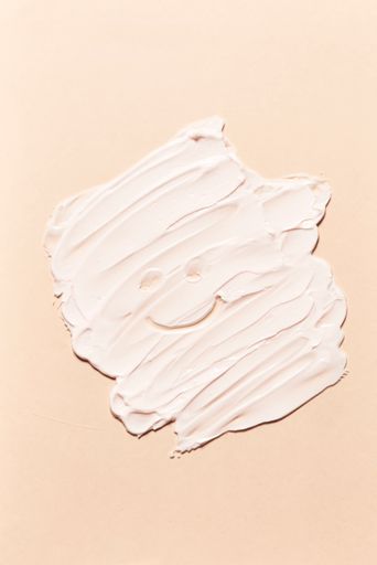 A vertical shot of a face cream smeared on a light pink background.