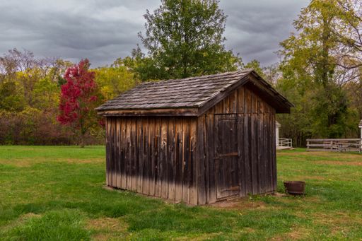 A beautiful shot of a wooden barn in a farm with a background of fall forest and cloudy sky.