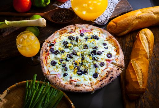 A top view of delicious Portuguese pizza with glasses of juice, bread, and vegetables on the table