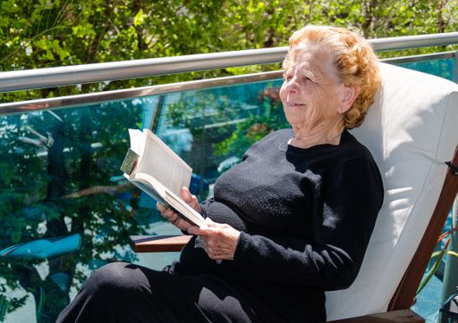 A Caucasian old woman sitting on a chair and reading a book