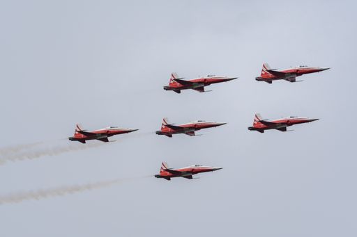 An air parade with red military aircraft flying in the blue clear sky
