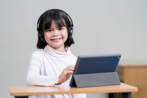 A closeup of the little girl sitting in front of the tablet with headphones. Online classes.