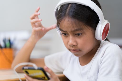 A closeup of the little girl with headphones looking at the smartphone.