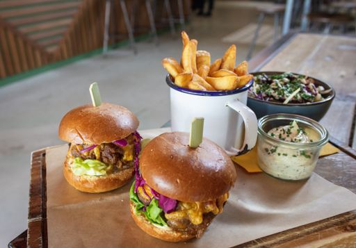 A high angle shot of hamburgers and fries in a cup with a salad and a sauce on the wooden tray with a blurred background