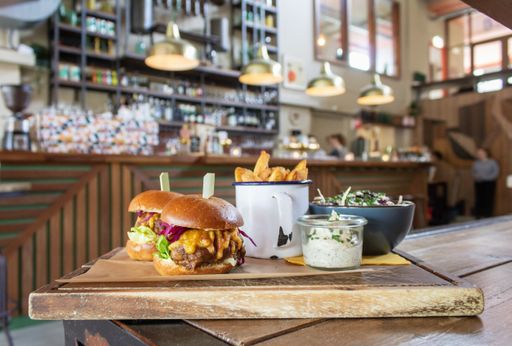 A closeup of hamburgers with fries in a cup and sauce on a wooden tray with a blurred background