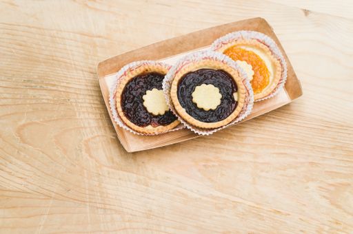isolated apricot and cherry jam tart in a paper backing cup on a wood tabletop background with text space