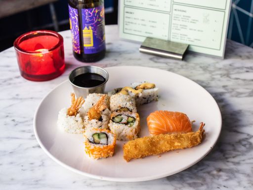 A close shot of sushi rolls with teriyaki sauce on a white round plate near a candle with a blurred background
