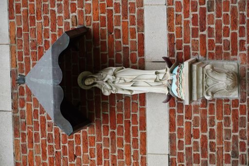 A vertical shot of the statue of the Virgin Mary against a red brick wall