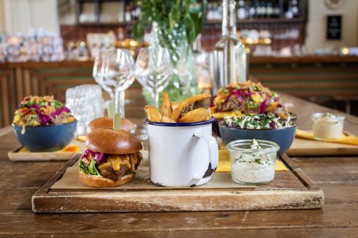 A close shot of hamburger near french fries in a cup and a sauce on a wooden tray with a blurred background