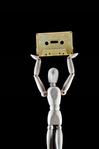 A human wooden dummy holding an old cassette tape above its head, isolated on black