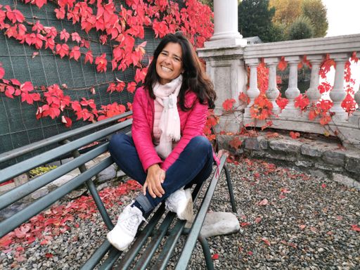 A smiling Hispanic female sitting on a bench on a balcony with girlish grapes