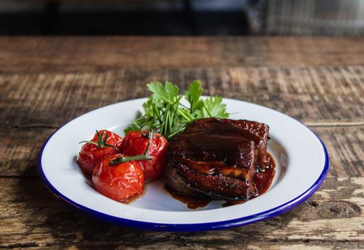 A close shot of meat with special sauce, tomatoes, and vegetables leaves on a white plate with a blurred background