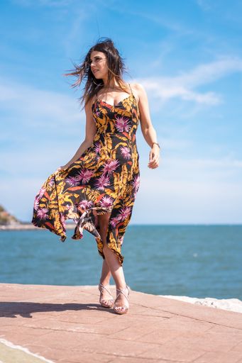 A vertical shot of a female in floral sundress captured by the ocean in San Sebastian, Spain