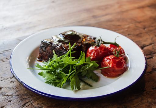 A close shot of meat with special sauce, tomatoes and vegetable leaves on a white plate