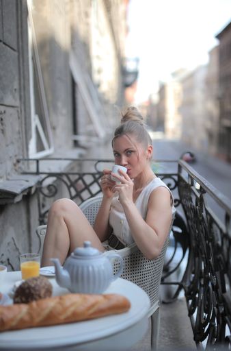 A vertical shot of a female sitting at a breakfast table on a balcony with a beautiful view