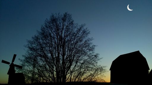 Silhouette of a windmill, tree, and barn against a twilight sky with a crescent moon.
