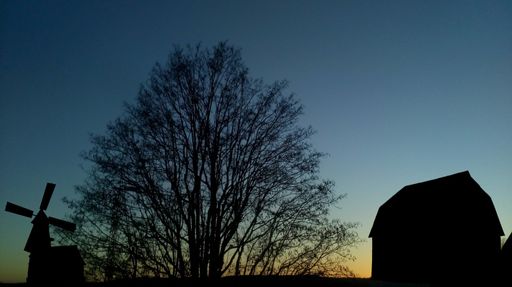 Silhouette of a tree, windmill, and barn against a twilight sky, showcasing rural tranquility.