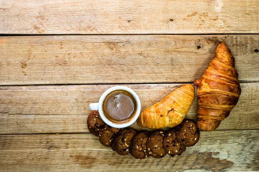 A top view of croissants, biscuits and a cup of coffee on a wooden board