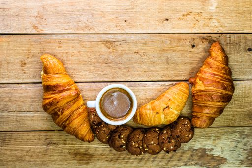 A top view of fresh croissants, biscuits, and a coffee cup on a wooden background with copy space. Coffee, food, and breakfast concept