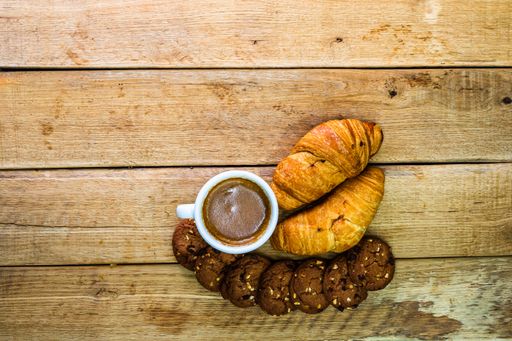 A top view of croissants, biscuits and a cup of coffee on a wooden board