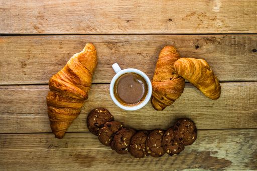 The fresh croissant, puff pastry, and biscuits are on a wooden table. Coffee, food, and breakfast concept.