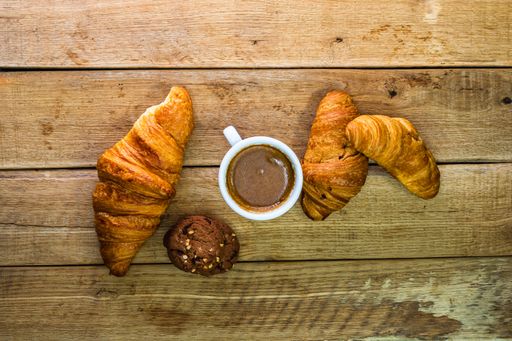 A top view of fresh croissants, biscuits, and a coffee cup on a wooden table