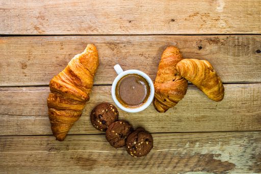 A top view of a fresh croissant with biscuits and coffee on a wooden table