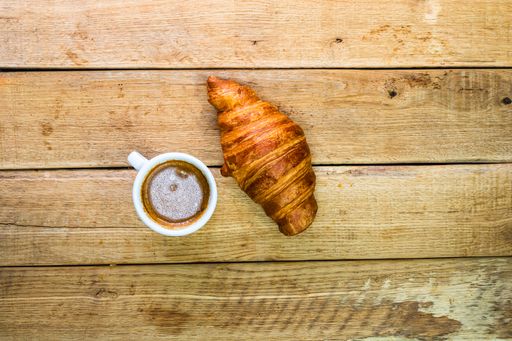 A top view of freshly baked croissant and a cup of coffee on wooden table
