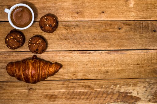 A top view of a cup of coffee, fresh croissant, and biscuits on a wooden background with a copy space. Coffee, food, and breakfast concept