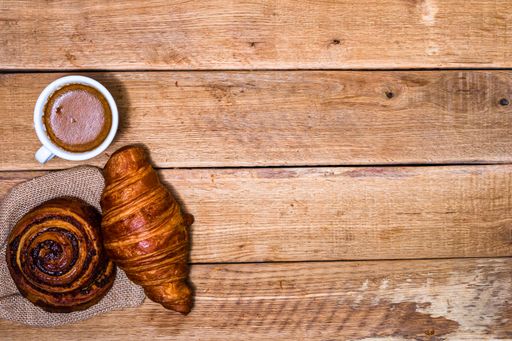 A top view of a fresh croissant, snail bun, and a coffee cup on a wooden table