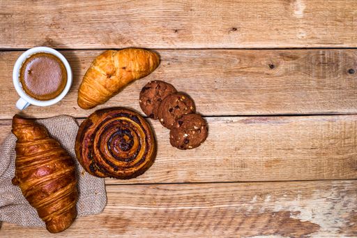A top view shot of fresh pastries, croissants, biscuits, and coffee on a wooden table