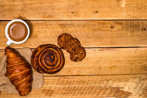 A top view shot of fresh pastries, croissants, biscuits, and coffee on a wooden table