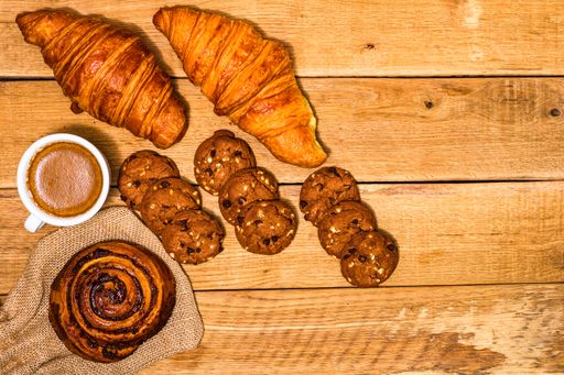 A top view shot of fresh pastries, croissants, biscuits, and coffee on a wooden table